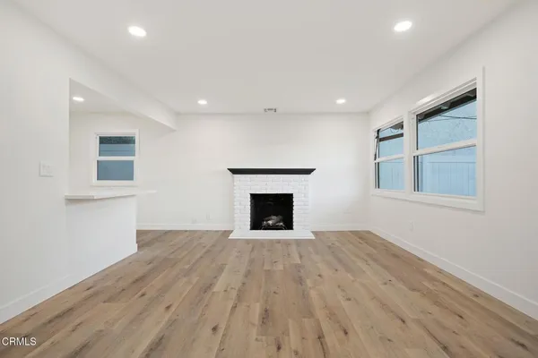 a view of an empty room with wooden floor fireplace and a window