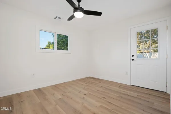 an empty room with wooden floor chandelier fan and windows