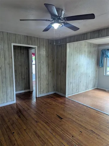 an empty room with wooden floor chandelier fan and windows