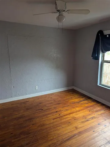 an empty room with wooden floor fan and windows