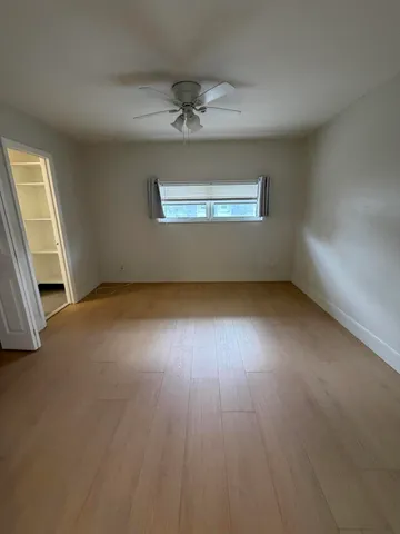 an empty room with wooden floor ceiling fan and windows