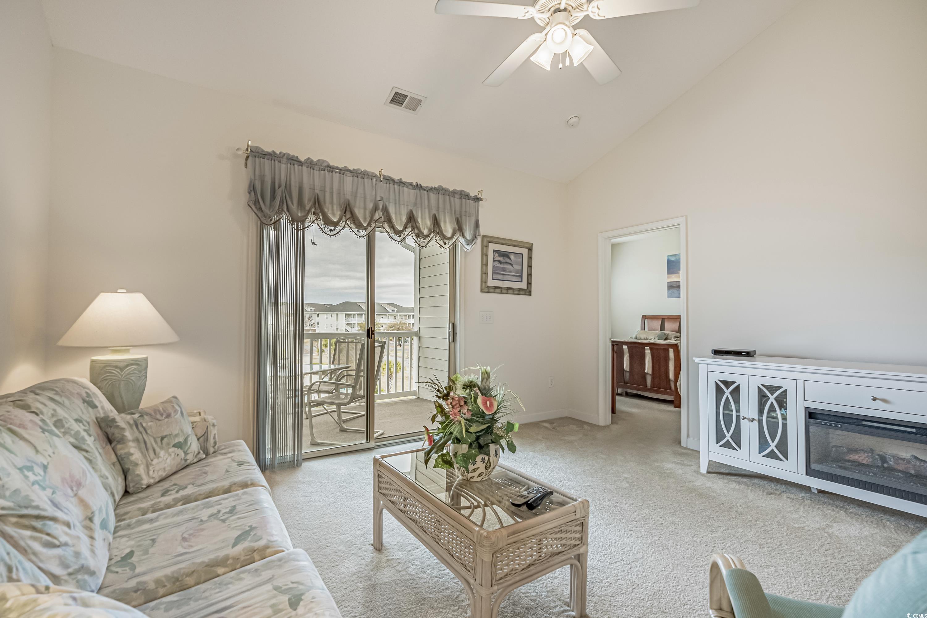 500 Wickham Drive, Unit HEATHERSTONE BUILDING 12 Myrtle Beach, SC 29579 - Photo 6 of 32 Living room featuring light carpet, a ceiling fan, a glass covered fireplace, and high vaulted ceiling