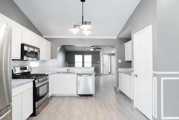 a kitchen with stainless steel appliances granite countertop a refrigerator a sink dishwasher a stove and white countertops with wooden floor