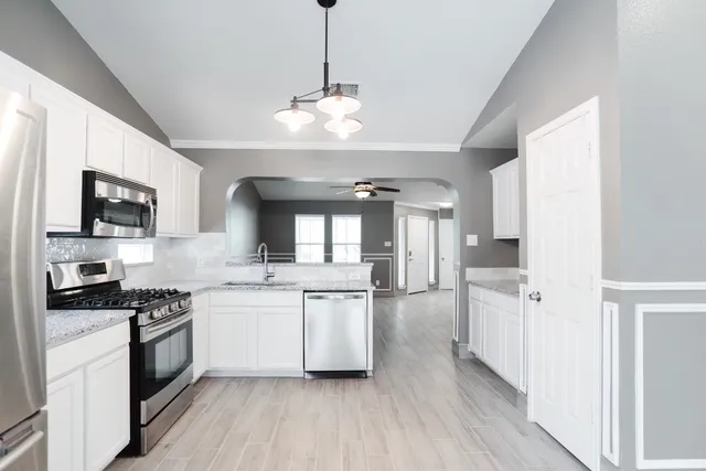 a kitchen with stainless steel appliances granite countertop a refrigerator a sink dishwasher a stove and white countertops with wooden floor