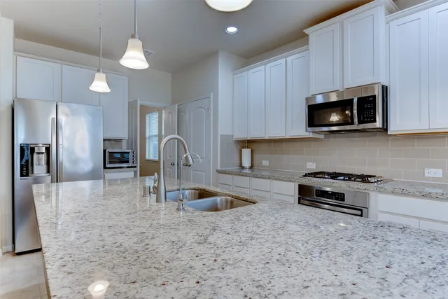 a kitchen with granite countertop a stove a microwave a sink a refrigerator and cabinets