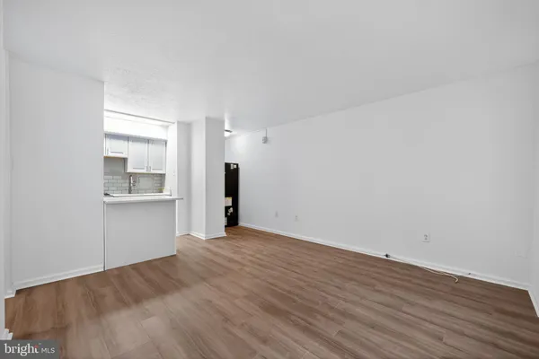 a view of an empty room with wooden floor and a kitchen