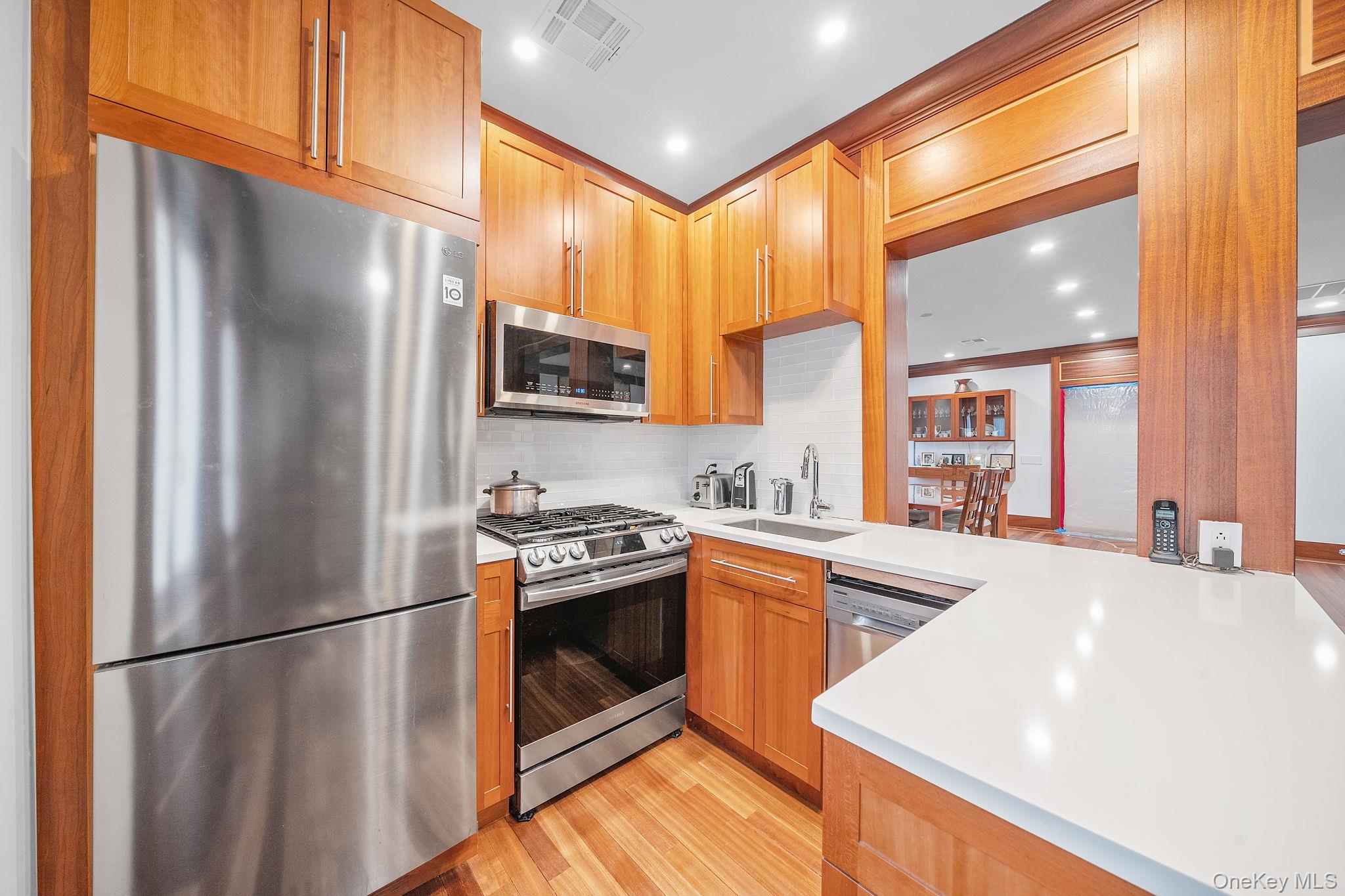 181 Walnut Street Lynbrook, NY 11563 - Photo 14 of 46 Kitchen featuring appliances with stainless steel finishes, light wood finished floors, recessed lighting, decorative backsplash, and brown cabinetry