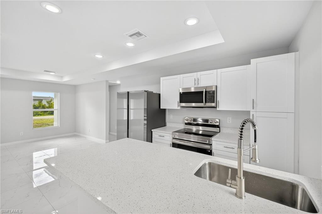 321 Ranier Avenue Lehigh Acres, FL 33974 - Photo 8 of 40 a kitchen with stainless steel appliances a stove a microwave a refrigerator a sink and white cabinets with wooden floor