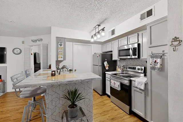 a kitchen with stainless steel appliances a stove a sink dishwasher a refrigerator white cabinets with wooden floor and cabinets