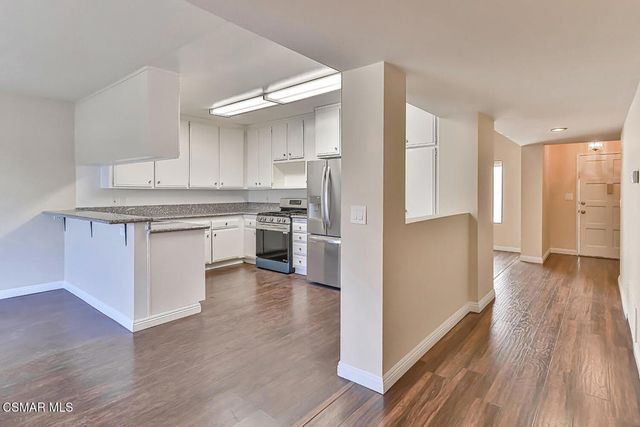 a large white kitchen with granite countertop a stove top oven a sink and white cabinets with wooden floor