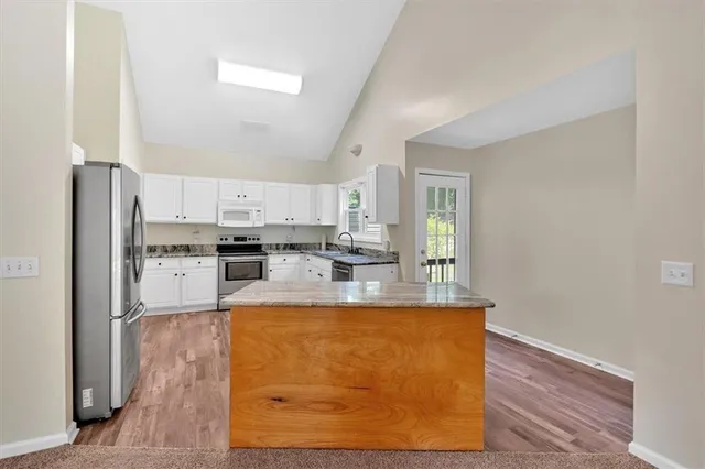 a large kitchen with stainless steel appliances granite countertop a refrigerator a stove and white cabinets with wooden floor