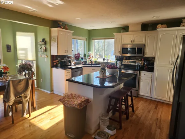 a kitchen with stainless steel appliances granite countertop a refrigerator a stove top oven a sink dishwasher and white cabinets with wooden floor