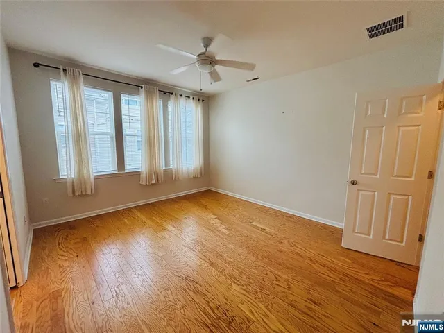 a view of an empty room with wooden floor and fan