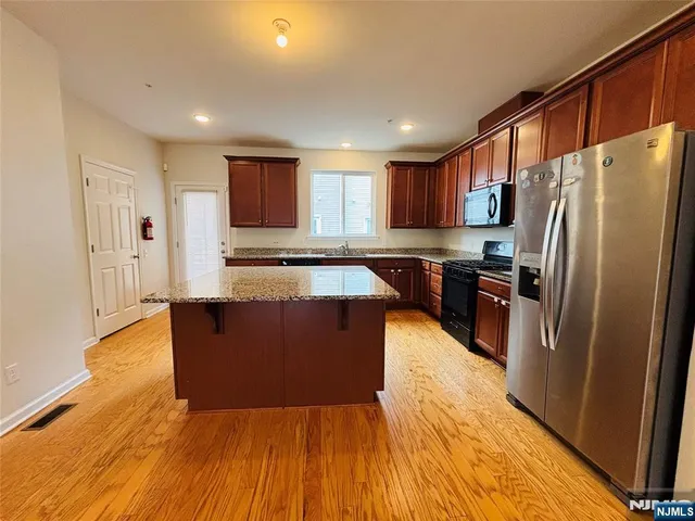 a large kitchen with stainless steel appliances granite countertop a refrigerator a sink dishwasher a stove and white countertops with wooden floor