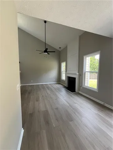 an empty room with wooden floor fireplace and windows