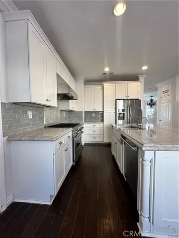 a kitchen with granite countertop white cabinets a sink dishwasher and a stove with wooden floor
