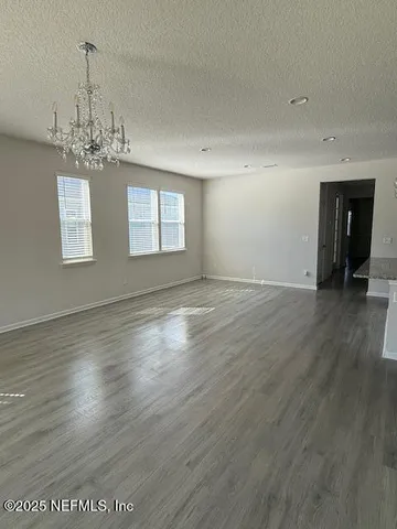 an empty room with wooden floor chandelier and windows