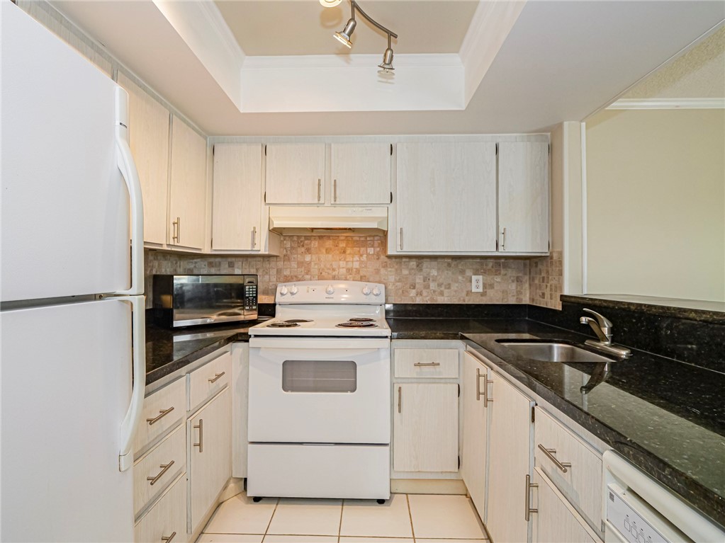 1860 Robalo Drive, Unit 105A Vero Beach, FL 32960 - Photo 4 of 35 a kitchen with granite countertop white cabinets sink and white appliances