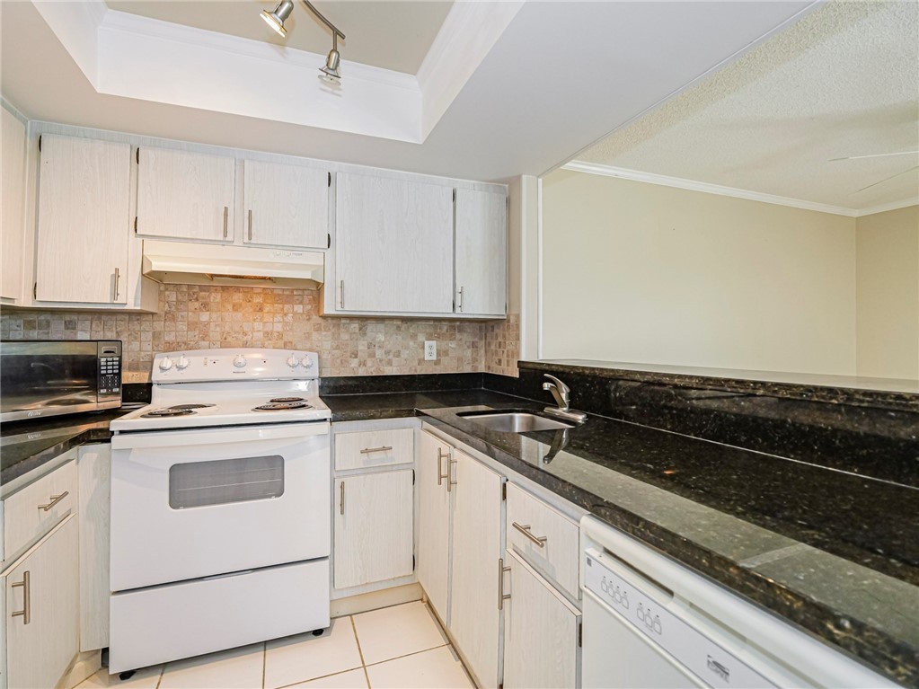 1860 Robalo Drive, Unit 105A Vero Beach, FL 32960 - Photo 5 of 35 a kitchen with granite countertop white cabinets and white appliances