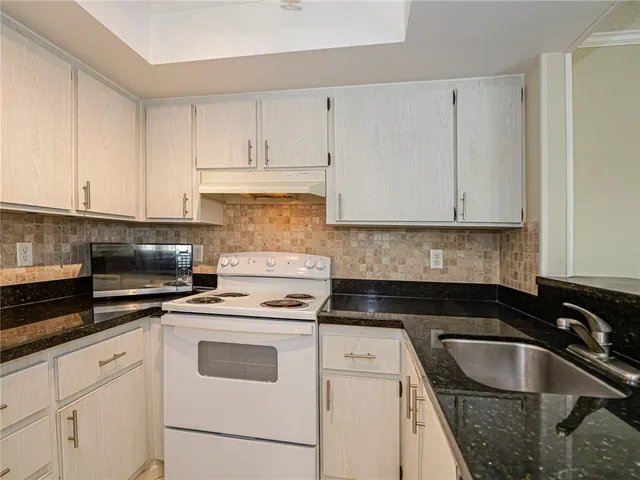 a kitchen with granite countertop white cabinets sink and stainless steel appliances