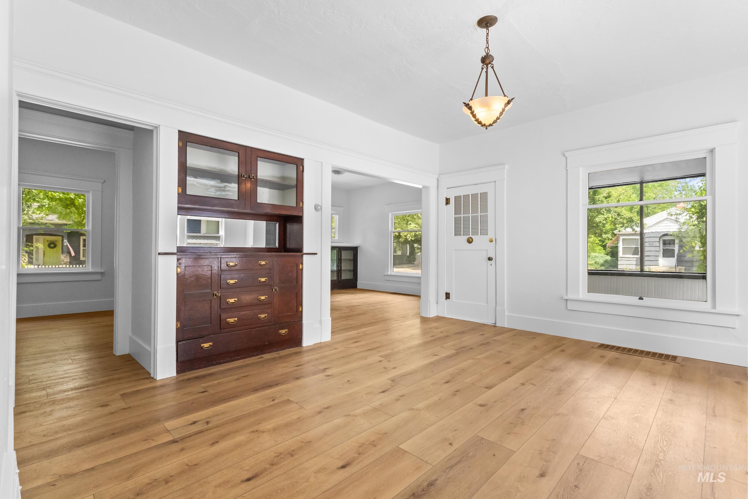 2119 West Brumback Street Boise, ID 83702 - Photo 8 of 30 Spacious room featuring light wood-finish flooring, a built-in dark wood cabinet with glass-front uppers, white trim, and a white paneled door with a grid-patterned glass insert