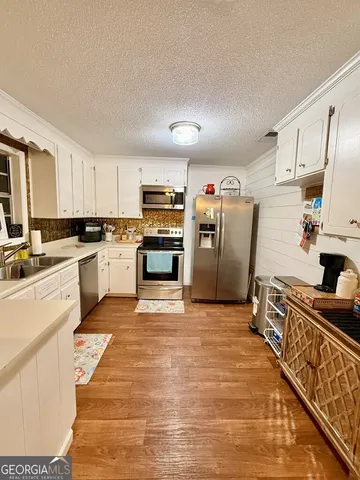 a large kitchen with stainless steel appliances granite countertop a stove top oven a sink dishwasher a refrigerator and white cabinets with wooden floor