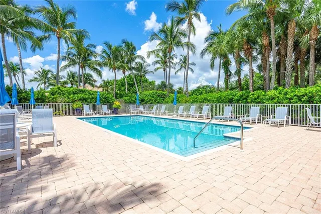 a view of swimming pool that has lawn chairs potted plants and palm trees
