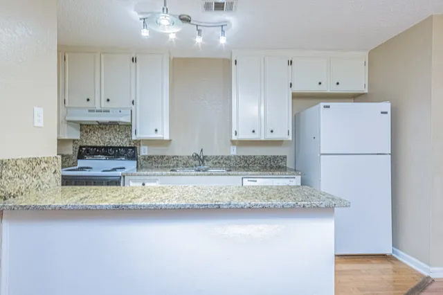 a kitchen with kitchen island granite countertop a refrigerator a stove a sink and white cabinets