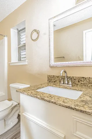 a bathroom with a granite countertop sink vanity mirror and toilet