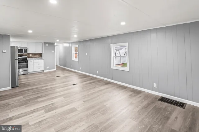an empty room with wooden floor kitchen view and windows