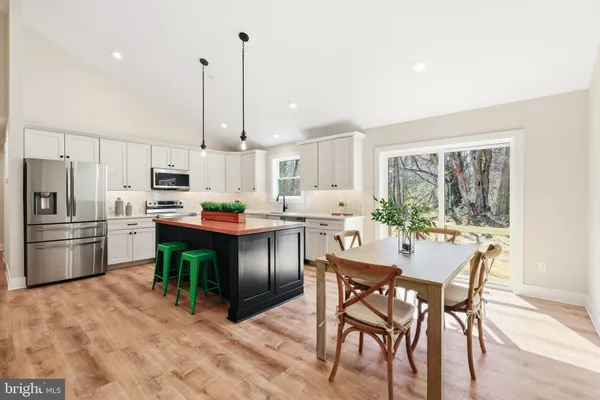 a kitchen with stainless steel appliances granite countertop a refrigerator a stove a sink a dining table and chairs with wooden floor
