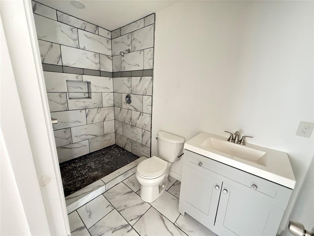 3233 Springview Avenue Dallas, TX 75216 - Photo 11 of 11 Shower with tiled walls and built-in niche, pebble-finish shower floor, white tiled flooring, and a vanity with an integrated sink