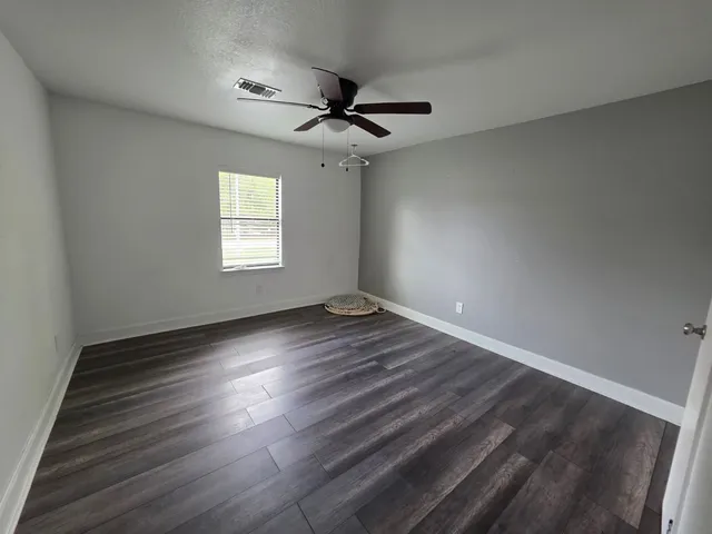 an empty room with wooden floor ceiling fan and windows