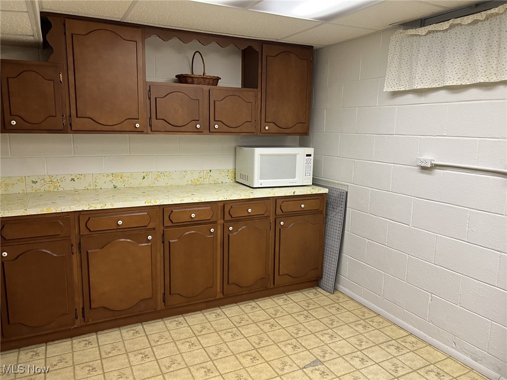 7579 McCreary Road Independence, OH 44131 - Photo 27 of 33 Craft room featuring concrete block wall, light countertops, light flooring, a drop ceiling, and white microwave