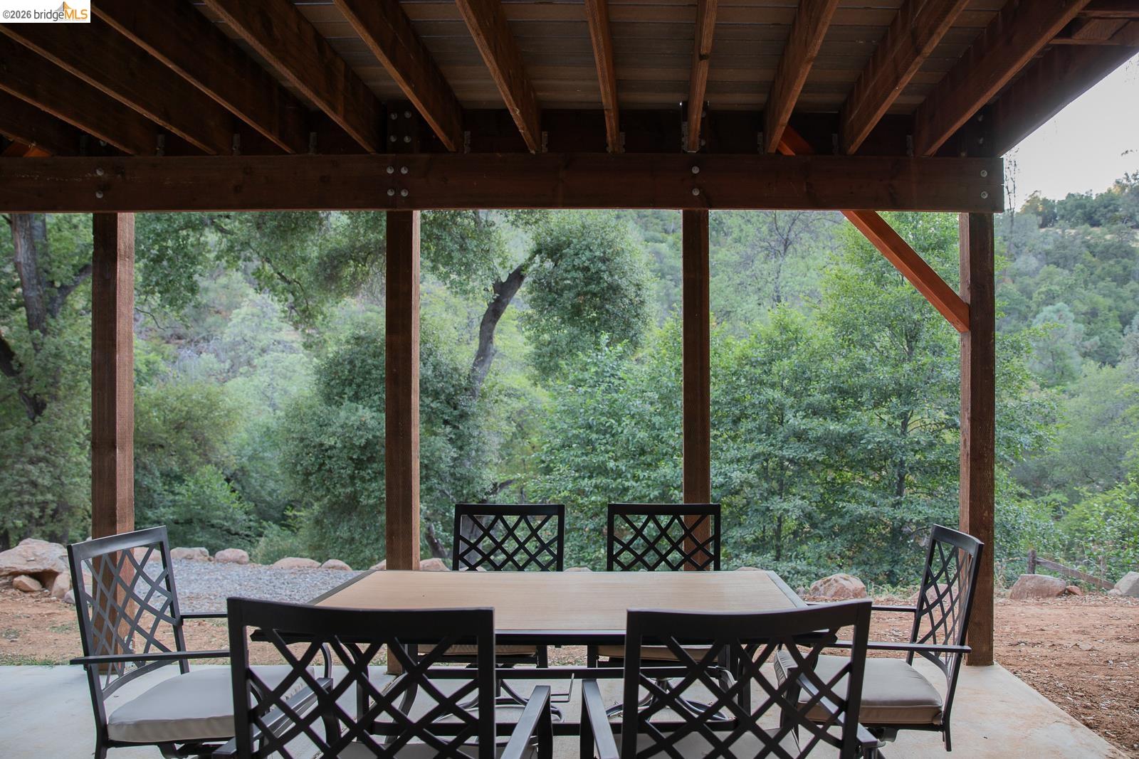 18399 Lime Kiln Road Sonora, CA 95370 - Photo 19 of 36 Covered outdoor patio with exposed wood beam ceiling, concrete flooring, and surrounding natural foliage