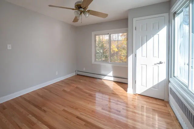 an empty room with wooden floor fan and windows