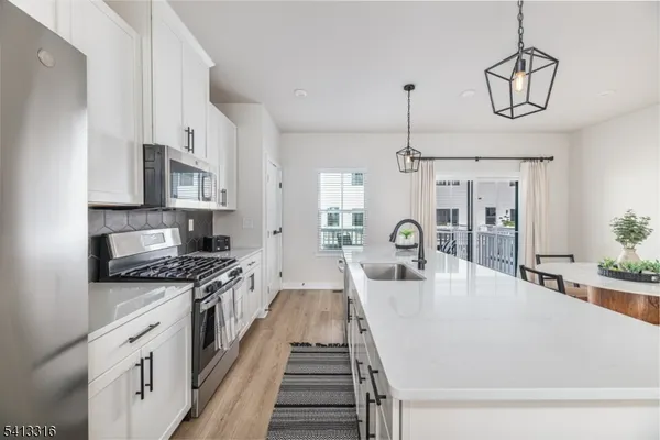 a large kitchen with stainless steel appliances granite countertop a stove a sink dishwasher and white cabinets with wooden floor