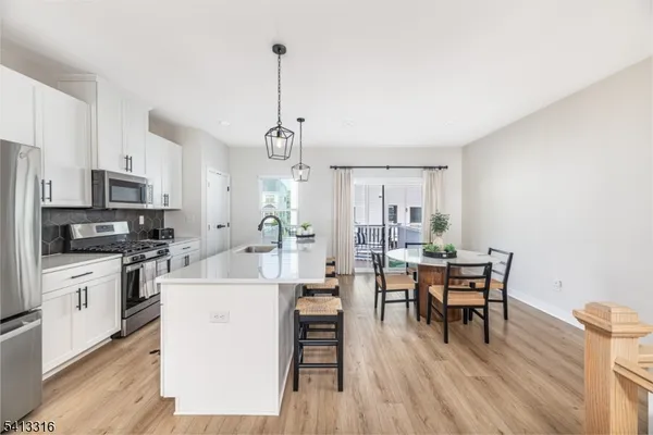 a kitchen with stainless steel appliances kitchen island granite countertop a stove top oven a sink a dining table and chairs with wooden floor