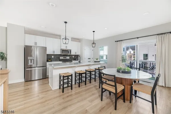 a kitchen with stainless steel appliances a dining table chairs stove refrigerator and cabinets