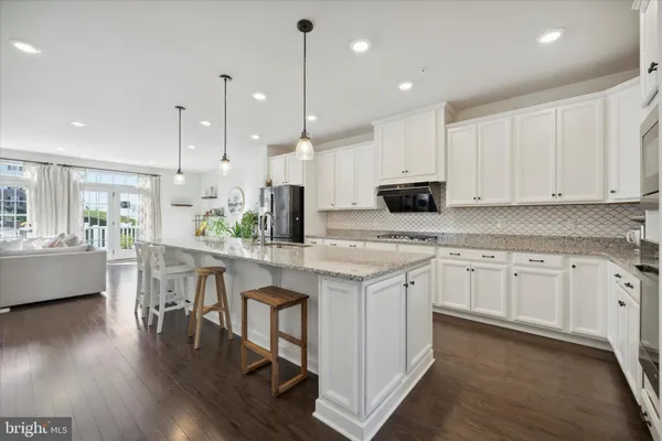 a kitchen with stainless steel appliances granite countertop a sink a stove a refrigerator and white cabinets with wooden floor