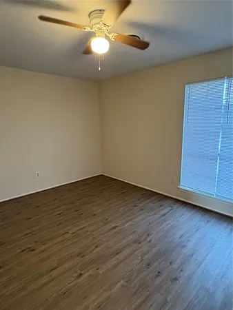 a view of an empty room with wooden floor and a ceiling fan