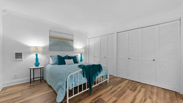 a bedroom with a bed a chair and potted plant on the wooden floor