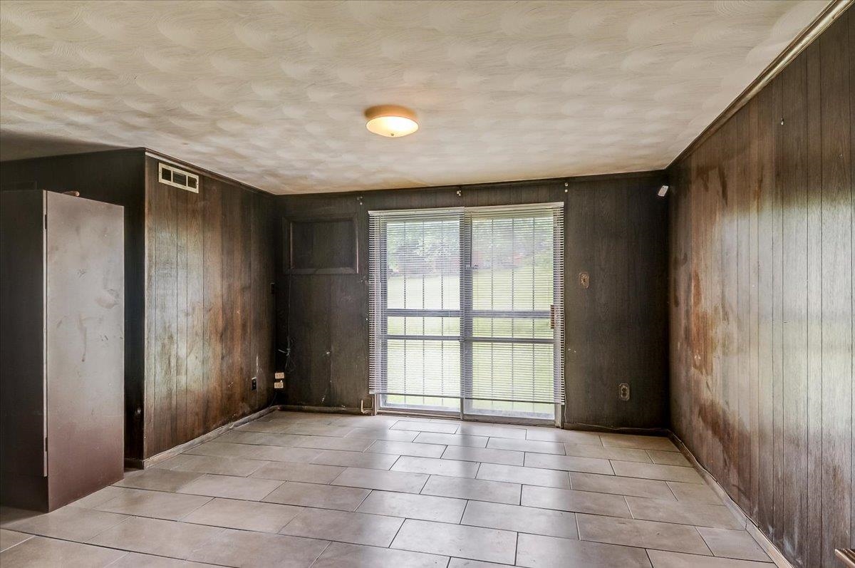 2569 Rozelle Street Memphis, TN 38114 - Photo 6 of 30 Interior room featuring a sliding glass door with security bars, vertical paneling on walls, a textured ceiling, and rectangular tile flooring