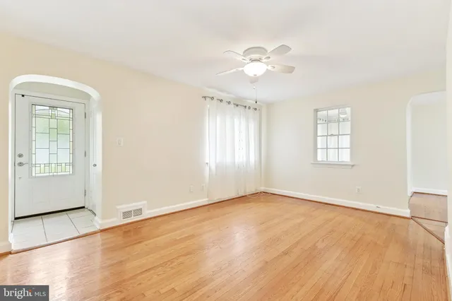 an empty room with wooden floor chandelier fan and windows