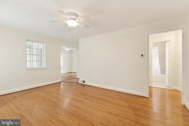 an empty room with wooden floor chandelier fan and windows