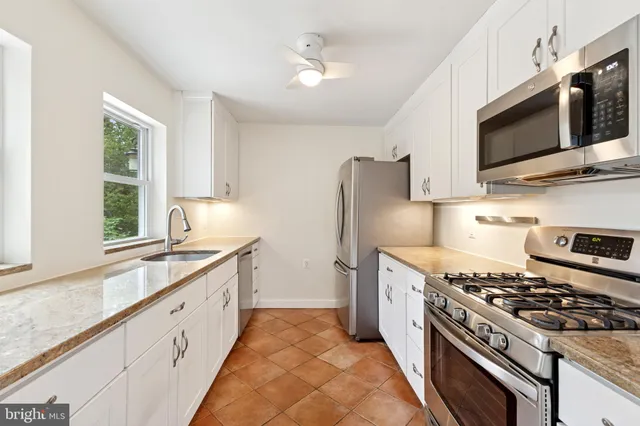 a kitchen with stainless steel appliances a sink a stove a microwave a refrigerator a window and cabinets