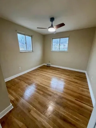 a view of an empty room with wooden floor and a ceiling fan