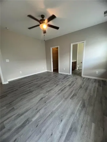 an empty room with wooden floor chandelier fan and windows
