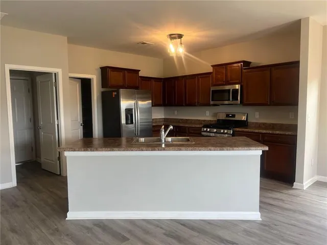 a view of a kitchen with stainless steel appliances granite countertop a stove top oven a sink and dishwasher a refrigerator with wooden floor