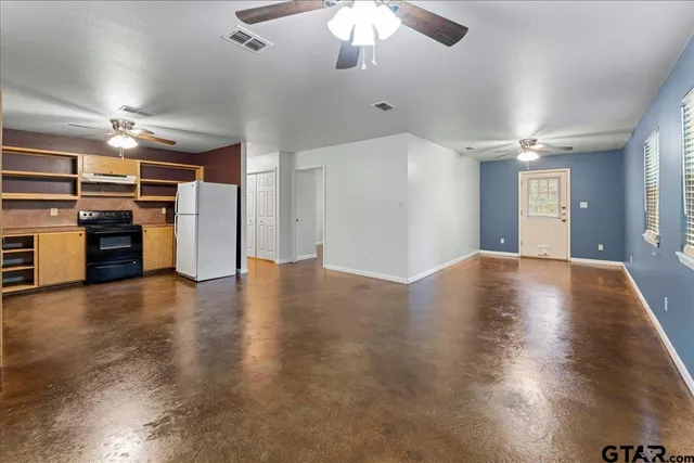an empty room with wooden floor kitchen view and a window